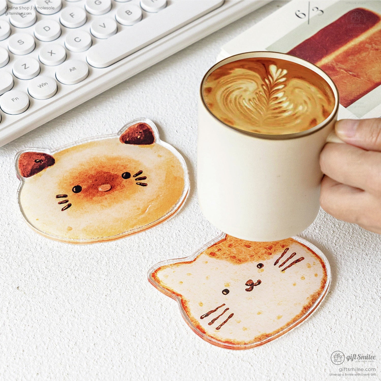 Two coasters, cat and bear bread designs, under a cup of coffee on a white desk
