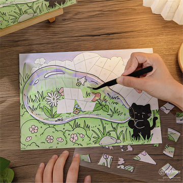 Person assembling a cute cat-themed mosaic puzzle on a wooden table, craft tweezers placing numbered pieces in a green garden scene.