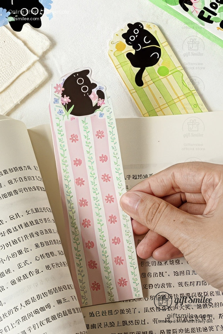 Cute black cat floral bookmark in pink and green, held in an open book  