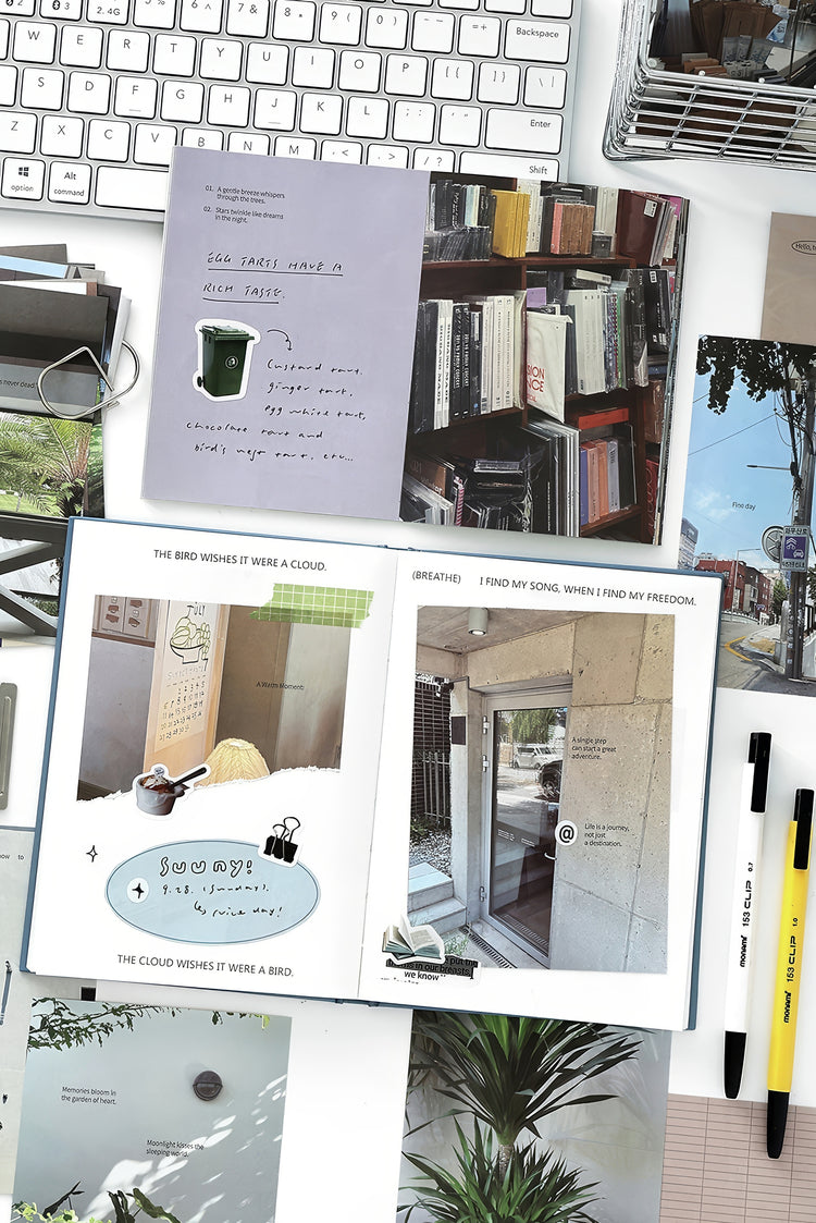 Open notebooks with colorful prints and photos black and yellow pens keyboard and wire basket on a white desk