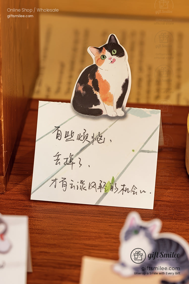 Tricolor catshaped paper stand on a white notecard with handwritten text displayed on a wooden surface