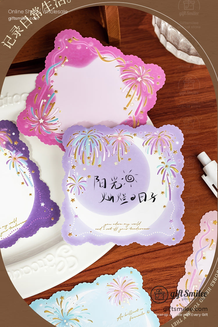 Pastel purple and pink fireworkthemed scallopededge sticky notes with gold accents on a wooden table