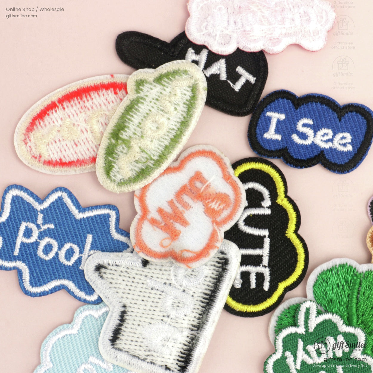 Assorted embroidered patches with colorful text designs including blue green black and red accents on a pink background