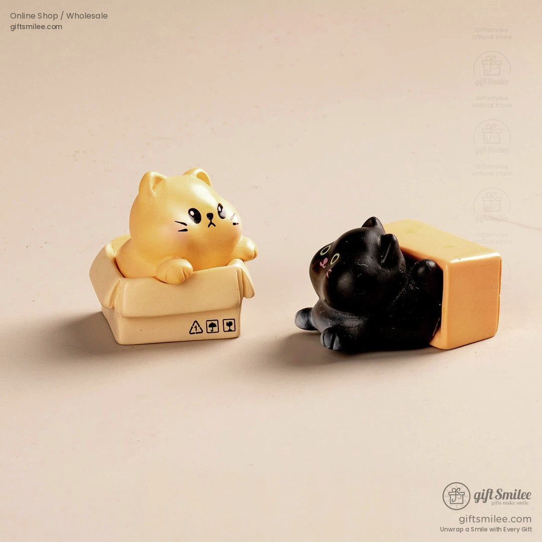Beige figurine of a yellow cat in a tiny box and black cat figurine partially inside a pastel orange box