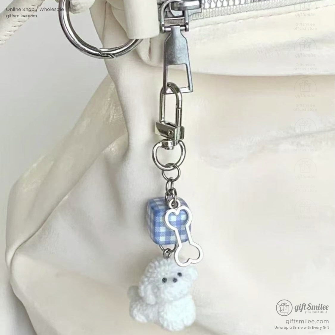 White plush poodle keychain with blue gingham cube charm and silver dog bone attached to a cream bag zipper pull