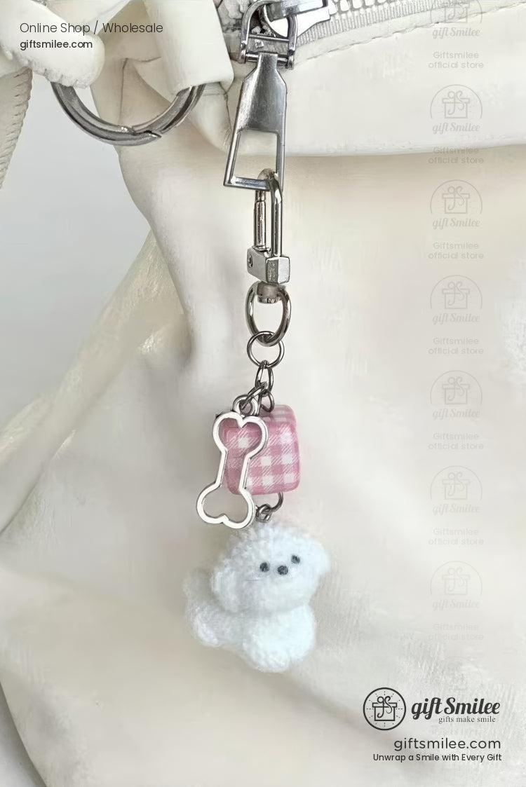 White plush dog keychain with silvertone hardware pink gingham charm and boneshaped pendant clipped to a white bag