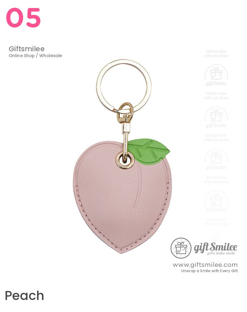 Pink faux leather peachshaped keychain with a green leaf accent and goldtone metal ring and clasp