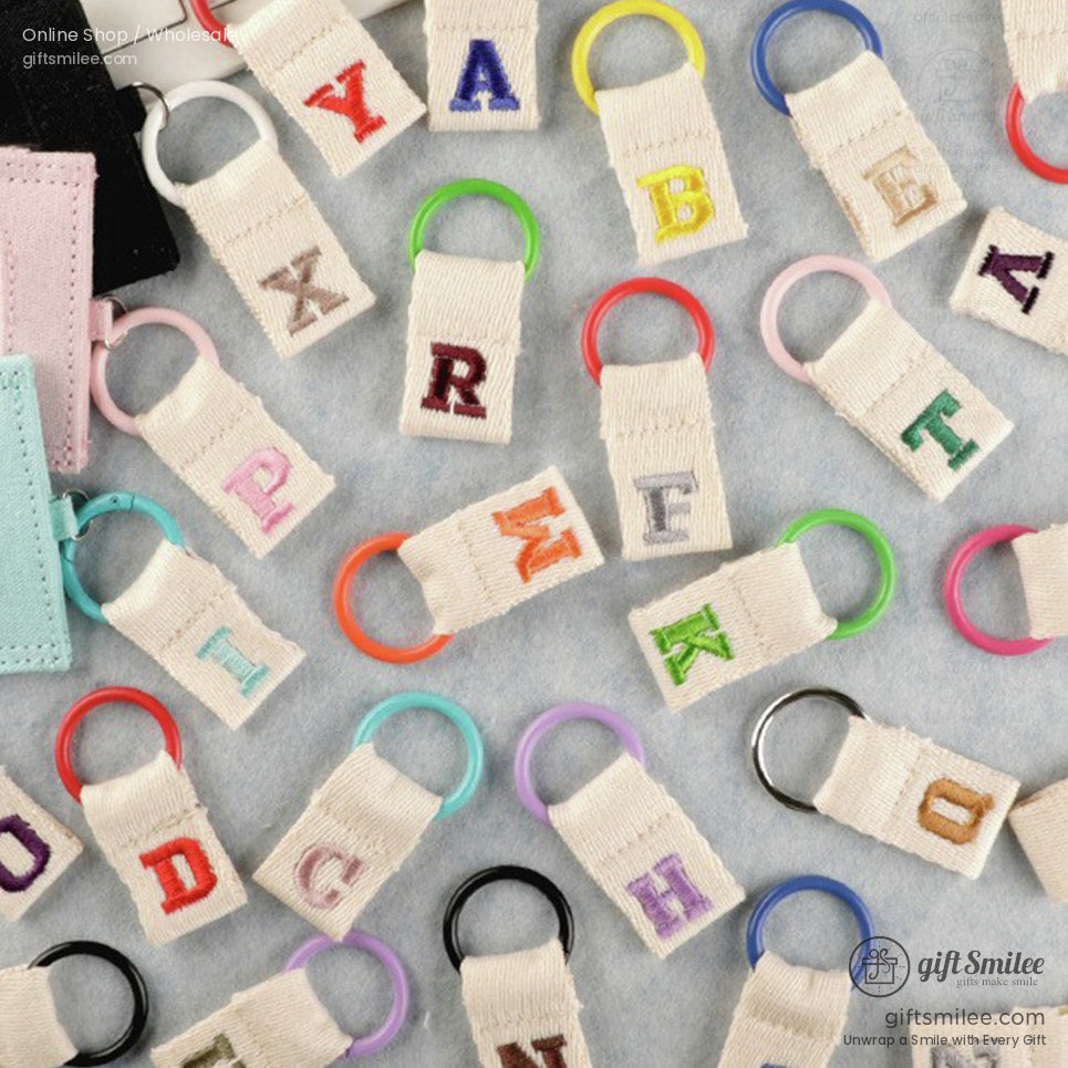 Multicolored embroidered alphabet keyrings with beige canvas tabs and vibrant circular rings on a light surface