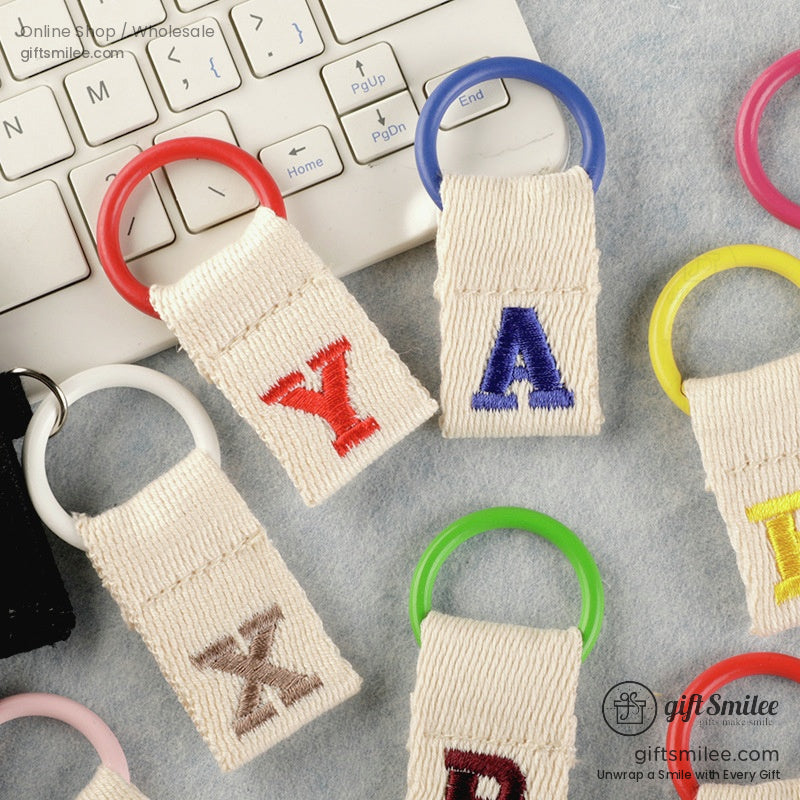 Multicolored plastic keyrings with beige cotton straps embroidered with bold colorful alphabet letters
