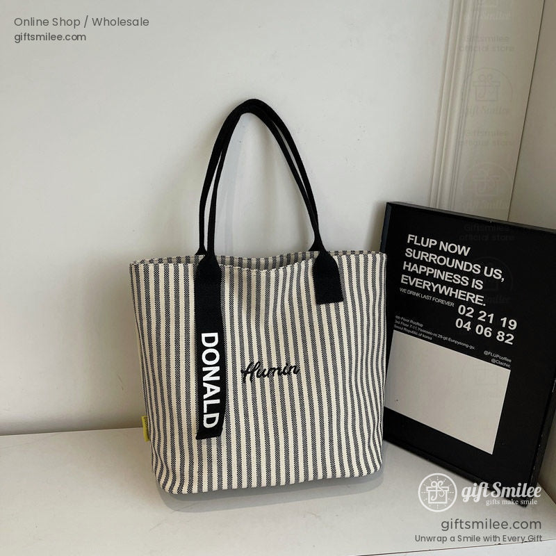 Black and white striped canvas tote bag with bold DONALD text black handles and minimal yellow accent