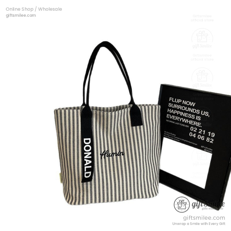 Beige and black striped fabric tote bag with black handles embroidered text and Donald printed on a strap