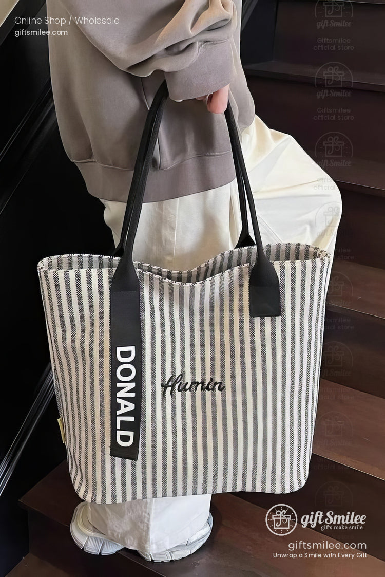 Beige and white striped tote bag with black handles embroidered human text and bold DONALD lettering on straps