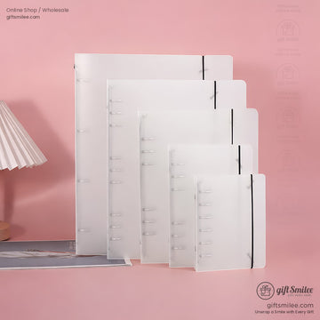 Translucent white plastic notebooks in various sizes with black elastic closures displayed against a pink background
