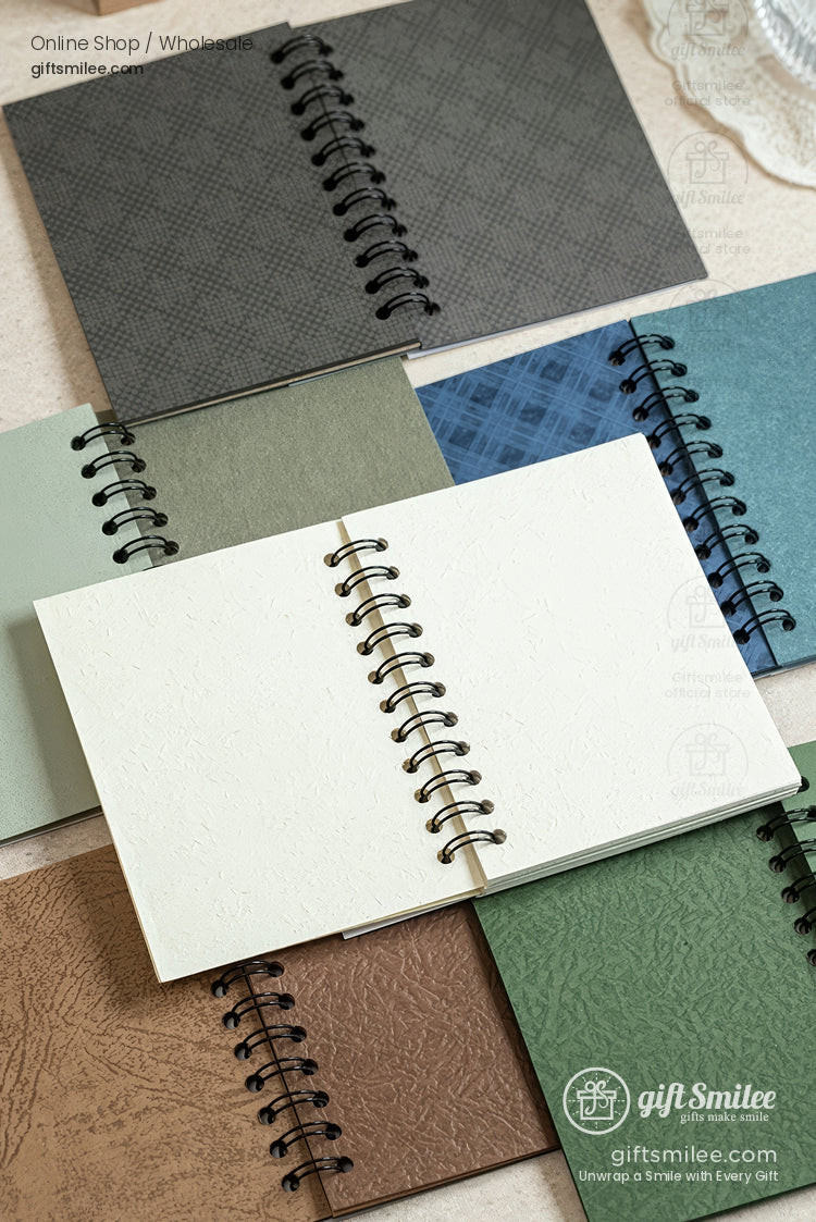Spiral-bound textured-cover notebooks in assorted earthy colors, open to blank pages, flat lay product photo for stationery store.