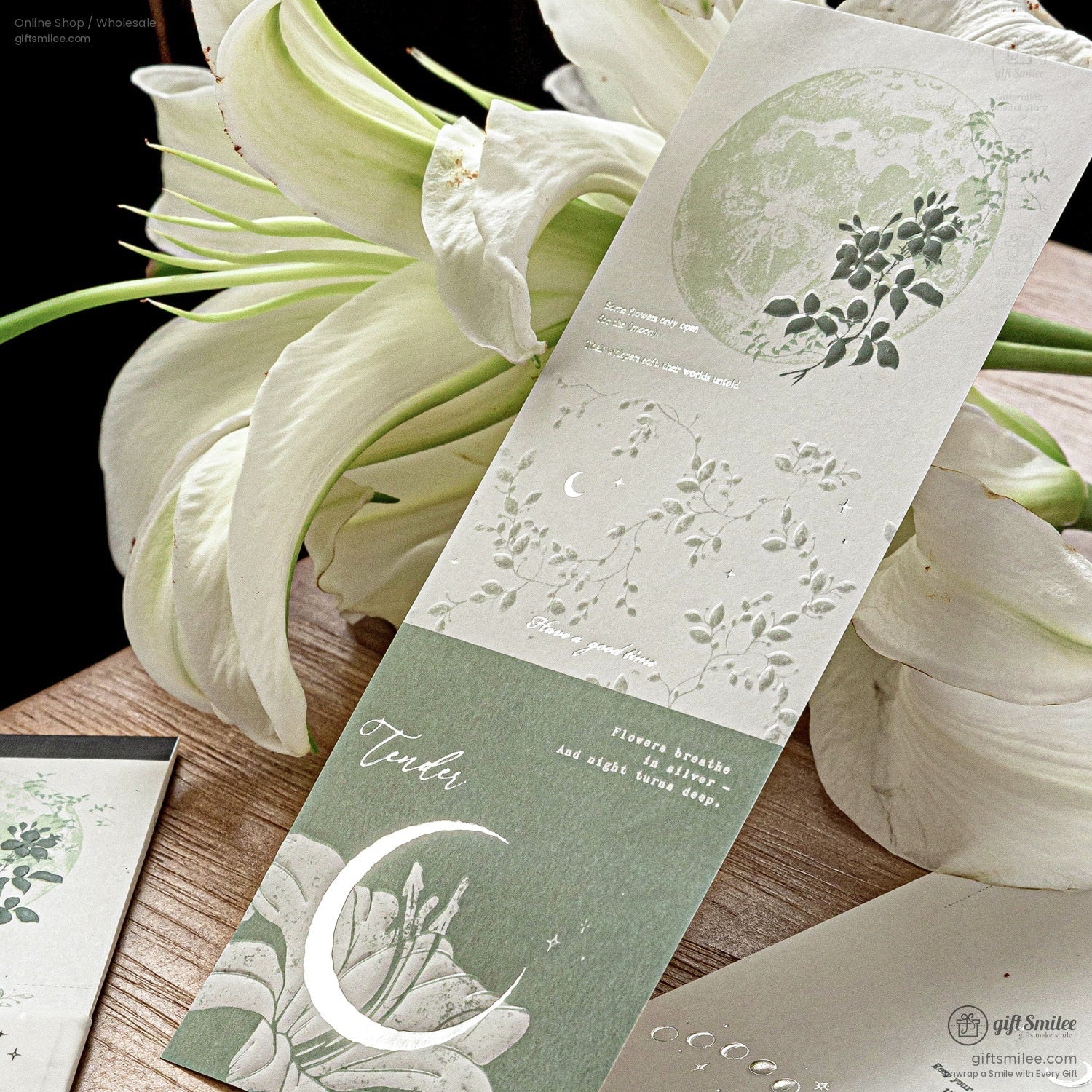 Elegant moon and lily-themed embossed bookmark on wood table with white lilies, green and cream aesthetic, stationery product for gift shop.