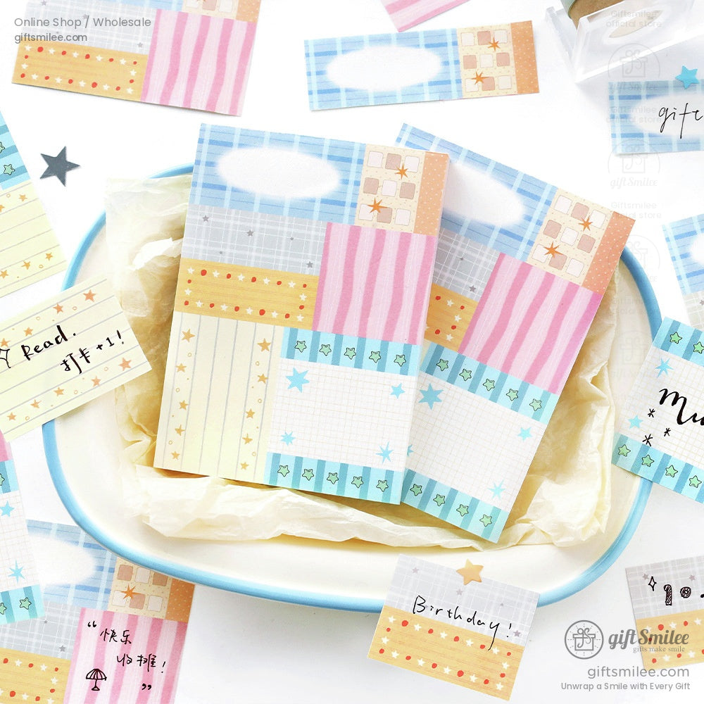 Pastelcolored memo pads with grid stripe and star patterns in blue pink and yellow tones arranged on a white tray