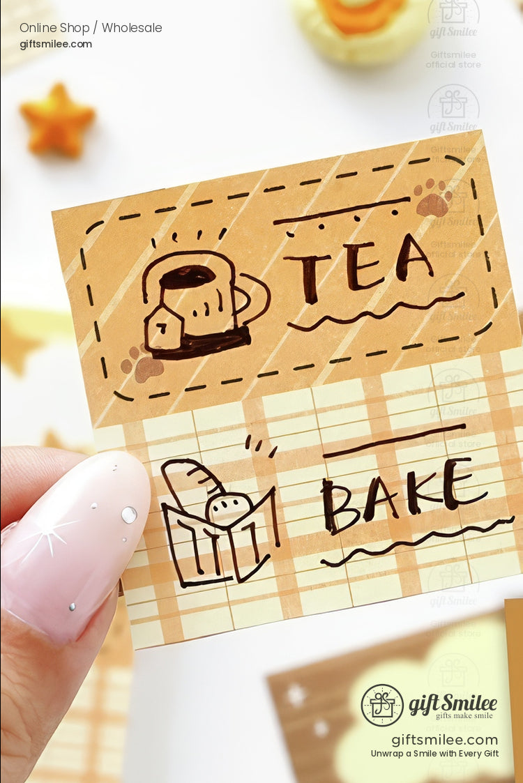 Hand holding brown and beige plaid sticky notes with doodles of a teacup bread loaf and text TEA and BAKE