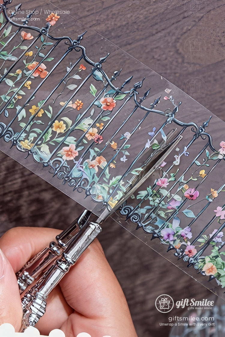 Transparent washi tape with vintage wrought-iron fence and pastel floral design being cut with scissors for scrapbooking crafts