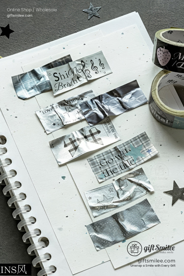 Silver and pastel decorative washi tapes displayed on a notebook, featuring metallic patterns, stars, and text labels, ideal for journaling or scrapbooking.