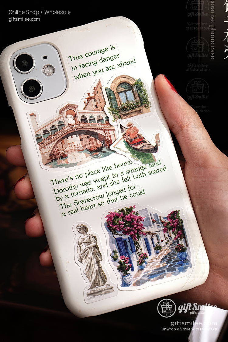 White iPhone case with vintage travel stickers and quotes, featuring European landmarks and floral street art, held in hand.