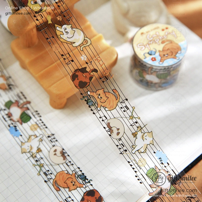 Transparent washi tape with playful orange white and brown cats on a musical staff with yarn and instruments