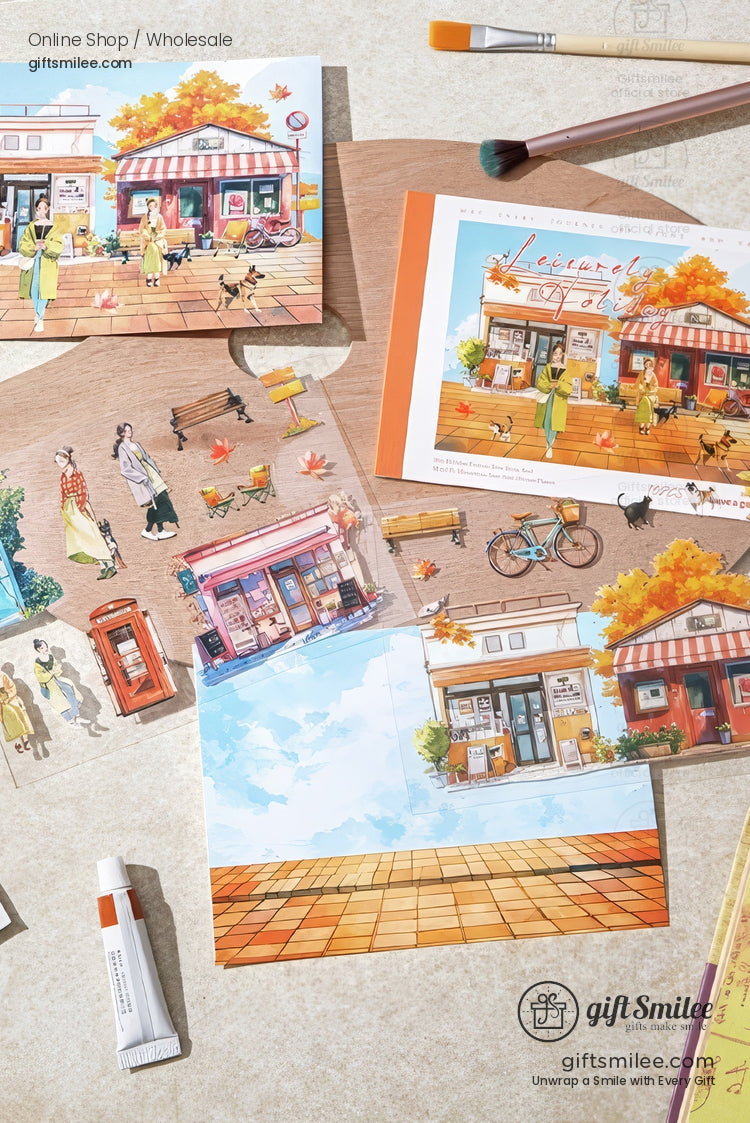 Autumn-themed stationery set with illustrated postcards and stickers of a cozy street shop scene, by giftSmilee, flat lay on a craft desk.