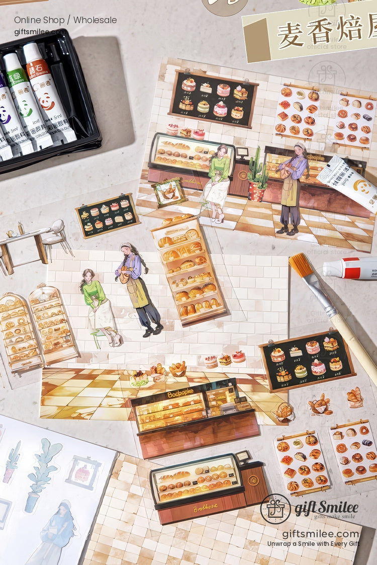 Bakery-themed sticker sheets with pastry display cases, bakers, and bread illustrations arranged on a craft desk with paints and a brush.