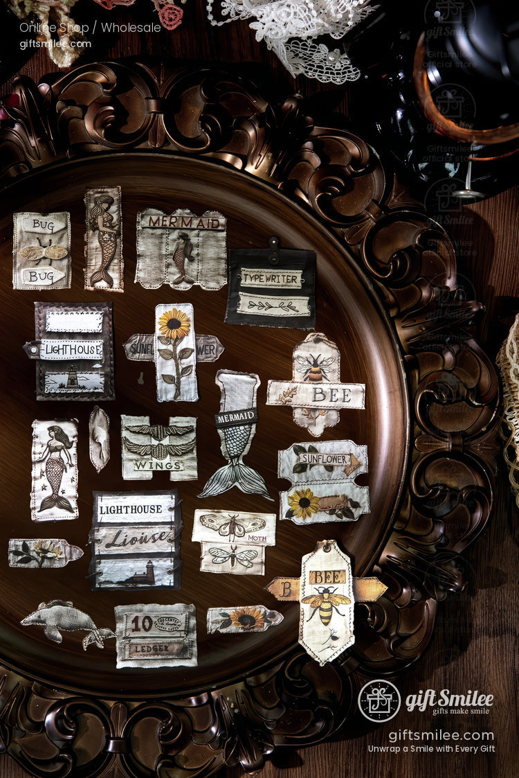 Vintage ephemera sticker set on ornate tray featuring lighthouse, mermaid, bee, sunflower, insect, and typewriter labels for scrapbooking and journaling
