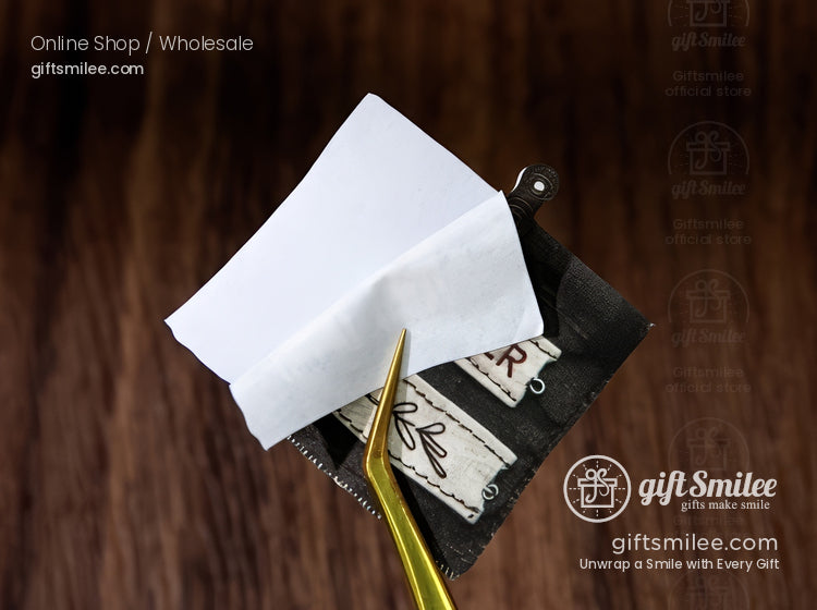 Gold tweezers lifting a blank white sticker label above rustic kraft tags on a wood background – GiftSmilee product photo for labels and packaging supplies.