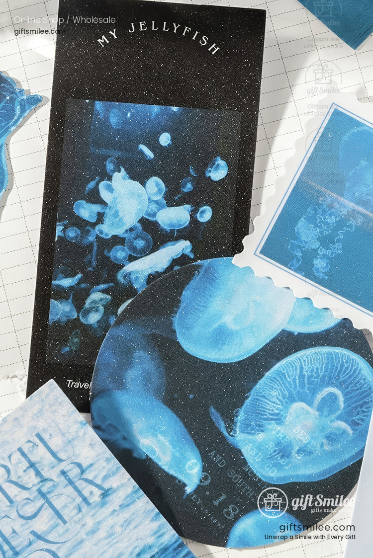 Assorted blue jellyfishthemed stationery with holographic details including stickers and a circular notebook on a grid background