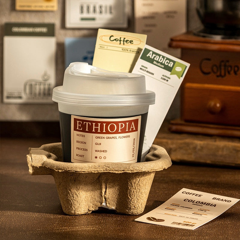 Assorted coffeethemed cards and labels in beige blue and yellow tones pinned on a corkboard with a retro green coffee grinder