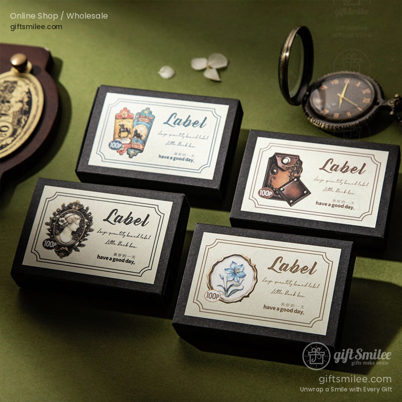 Black rectangular boxes with vintagestyle decorative labels featuring floral cameo and antiqueinspired designs