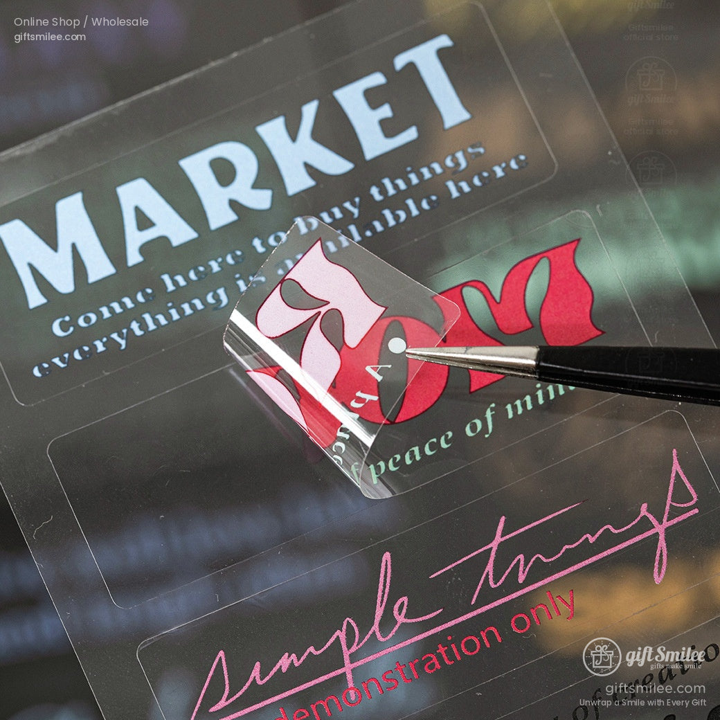 Clear adhesive label with bold red white and pink text design lifted by tweezers on a glossy background