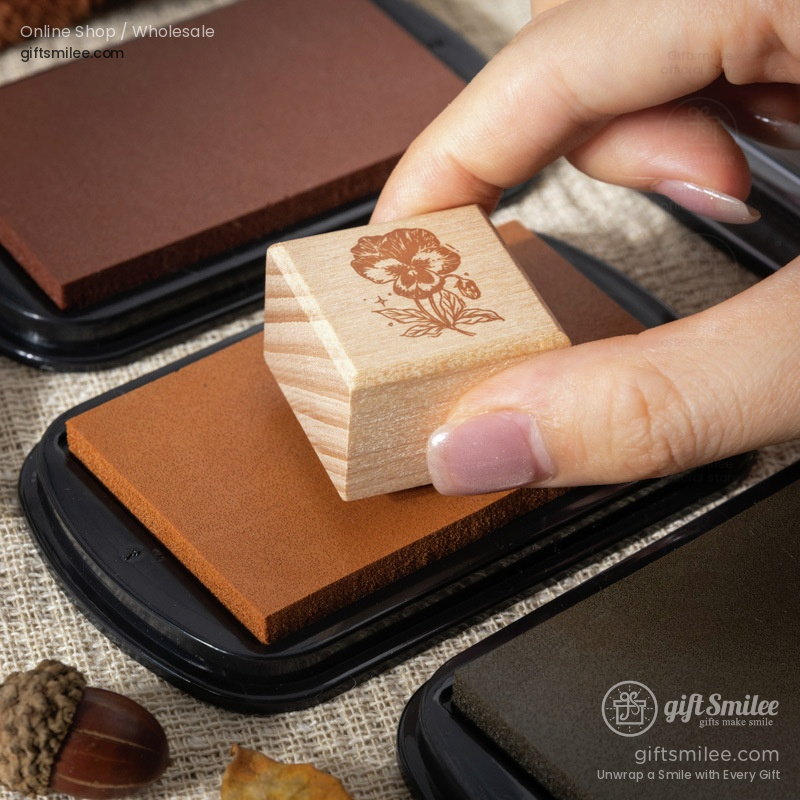 Hand pressing a floralpatterned wooden rubber stamp onto a brown ink pad set on a textured beige surface